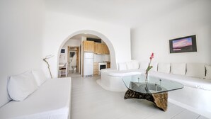 A modern living room with a glass coffee table, white sofas, and a kitchen in the background.