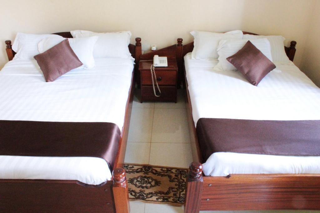 Cama doble con cabecera de madera, mesita de noche con teléfono y un cojín marrón.