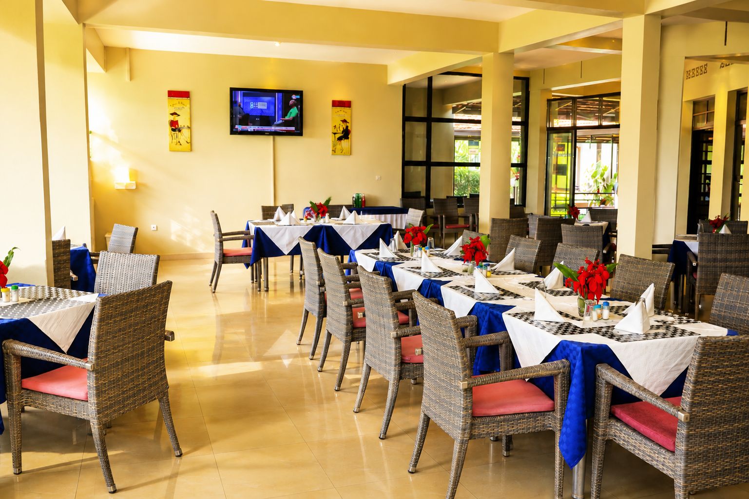 A dining area with tables set for service, wicker chairs, and a television mounted on the wall.