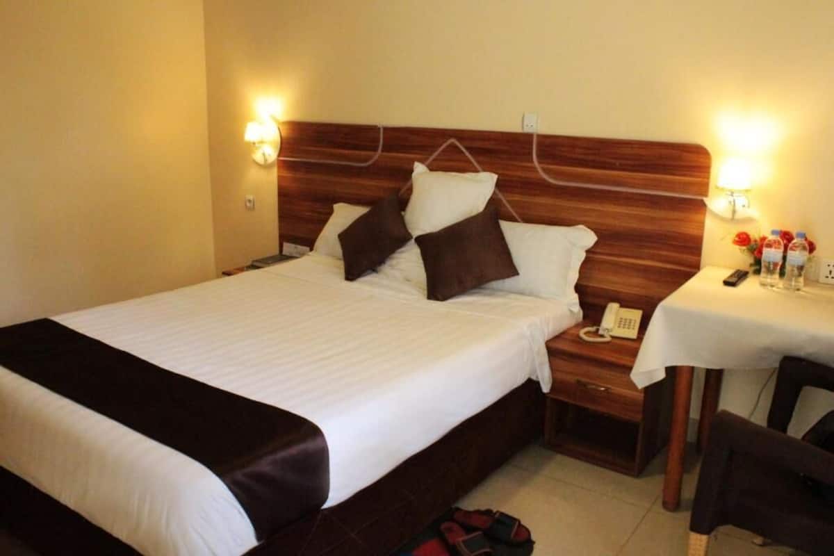 Una habitación de hotel con una cama grande, mesitas de noche, un escritorio con una silla y un teléfono.
