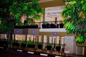 Un hotel de varios pisos con balcones, plantas en macetas y un letrero que indica una zona de estacionamiento.