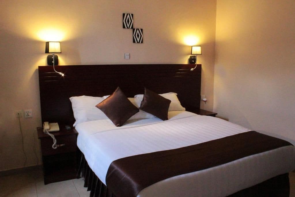 A hotel room with a large bed, two bedside lamps, a telephone, and a wall-mounted light fixture.