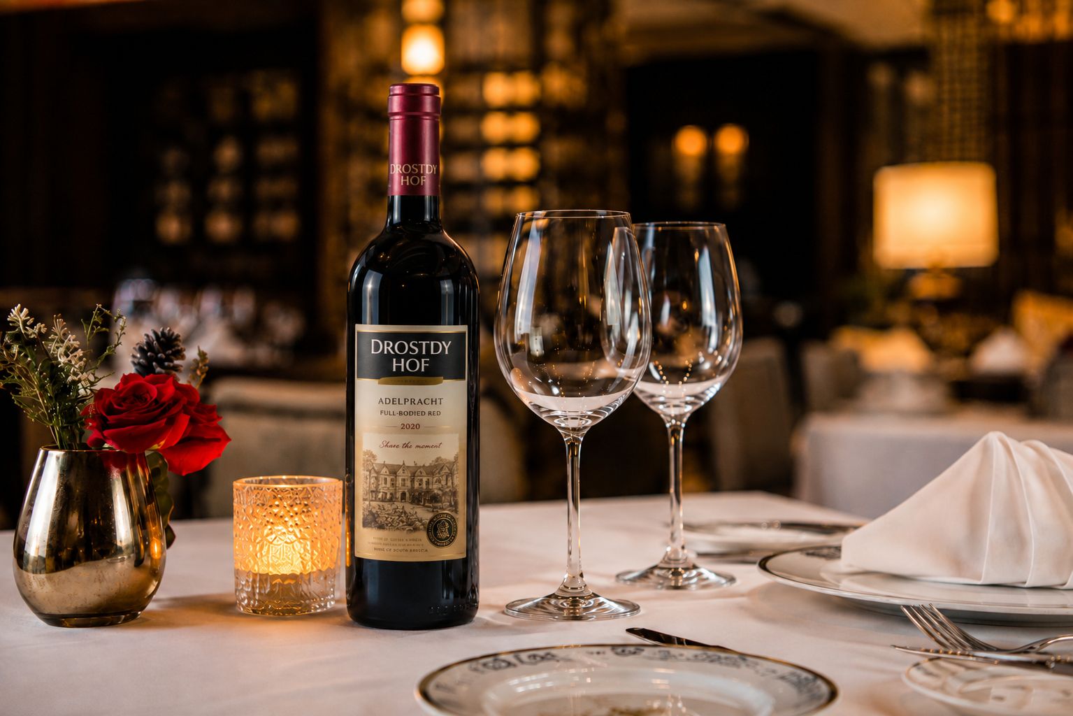 A table set for dining with a bottle of wine, glasses, a candle, and a vase with flowers.