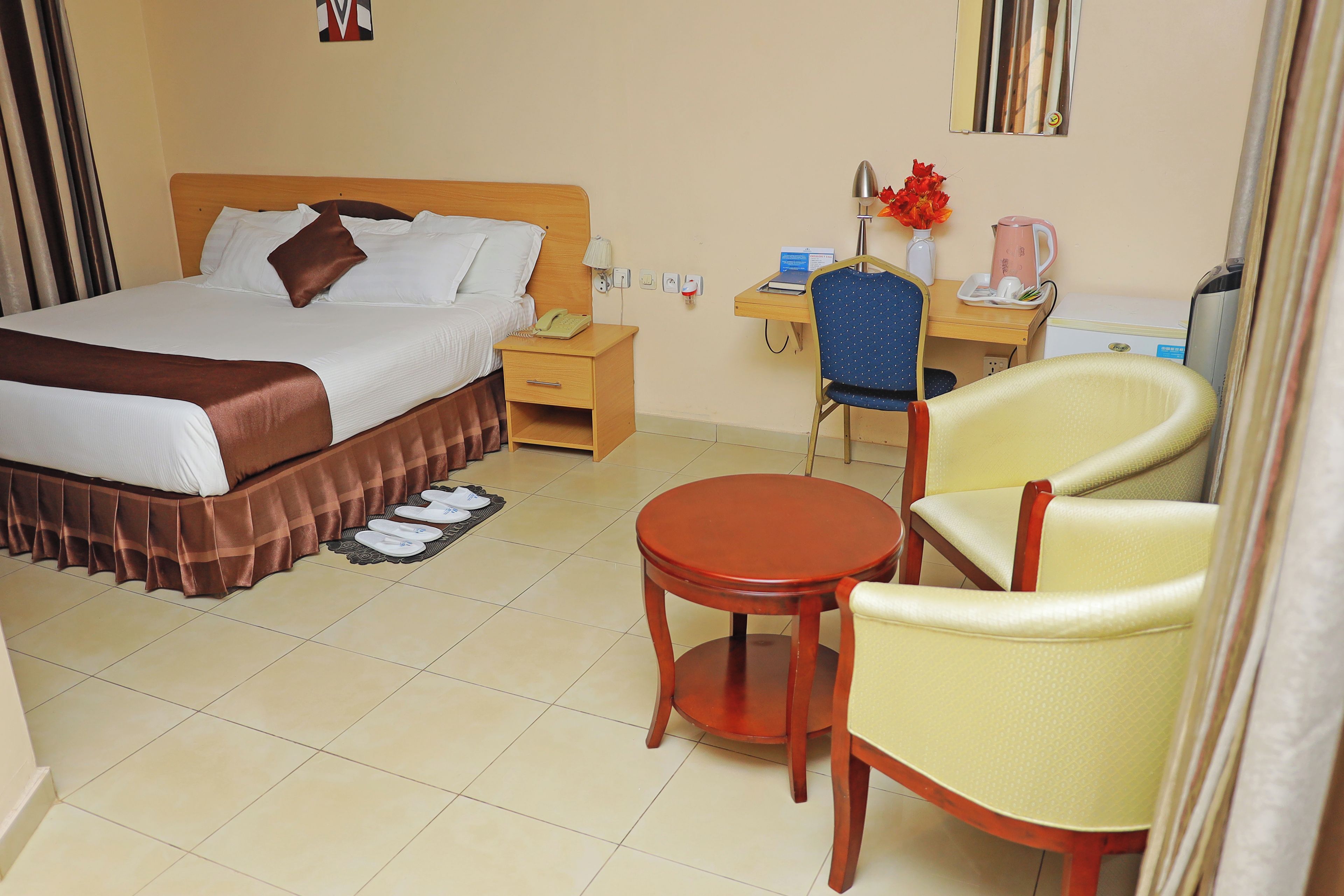 A hotel room with a bed, bedside table, desk, chair, and a small table.