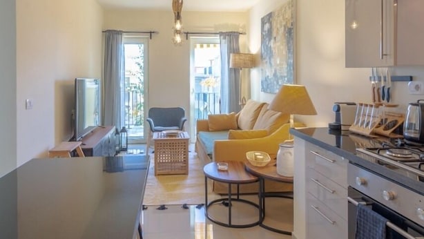 A modern kitchen with a central island, a dining area with a yellow sofa, and a TV in the living room. - Vesta - Sahl Hasheesh Residence (Hurghada)