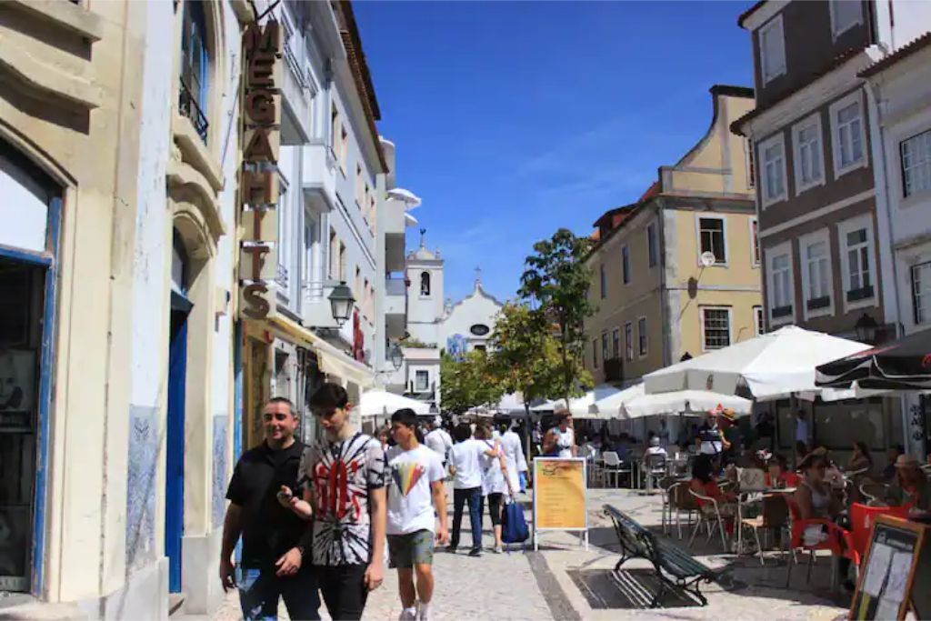 Eine Straße mit Gebäuden, Außenbestuhlung und Passanten.