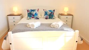 Een net opgemaakt bed met gestreepte lakens en twee decoratieve kussens, met nachtkastjes en lampen aan weerszijden.