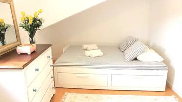 A small, neatly arranged bedroom with a bed, a dresser, a mirror, and a vase with flowers.