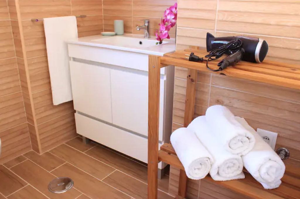 A bathroom with a wooden vanity, a sink, and a shelf with towels and a hairdryer.