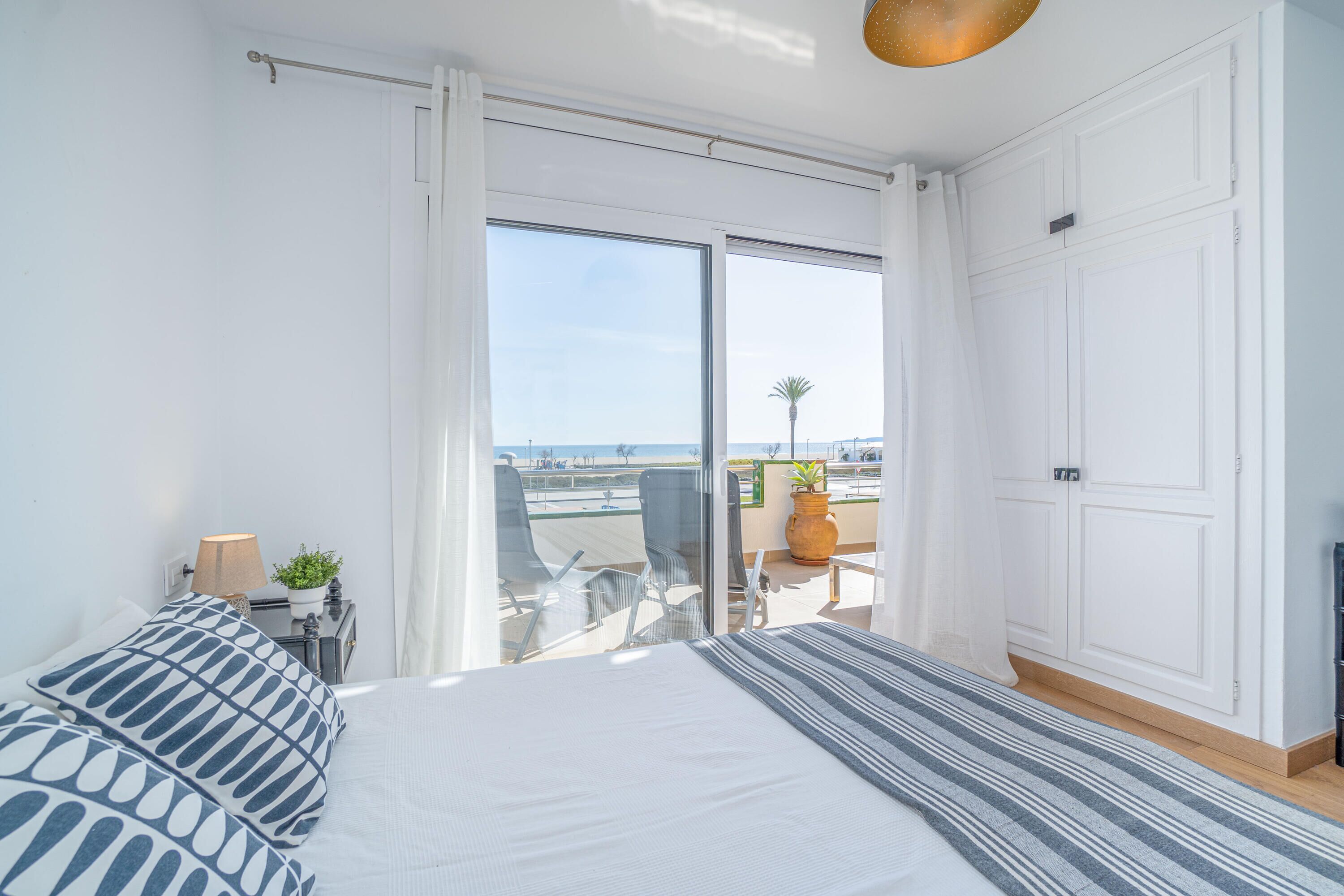 A bedroom with a large bed, a view of the beach, and a balcony with chairs and a table.