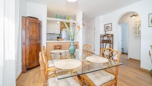 Een eetgedeelte met een glazen tafel, rieten stoelen en een houten kast.