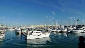 Un puerto deportivo con varias embarcaciones amarradas, cielo despejado y una persona visible en primer plano.