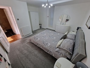 Une chambre à coucher avec un grand lit, une commode, un miroir et un radiateur.