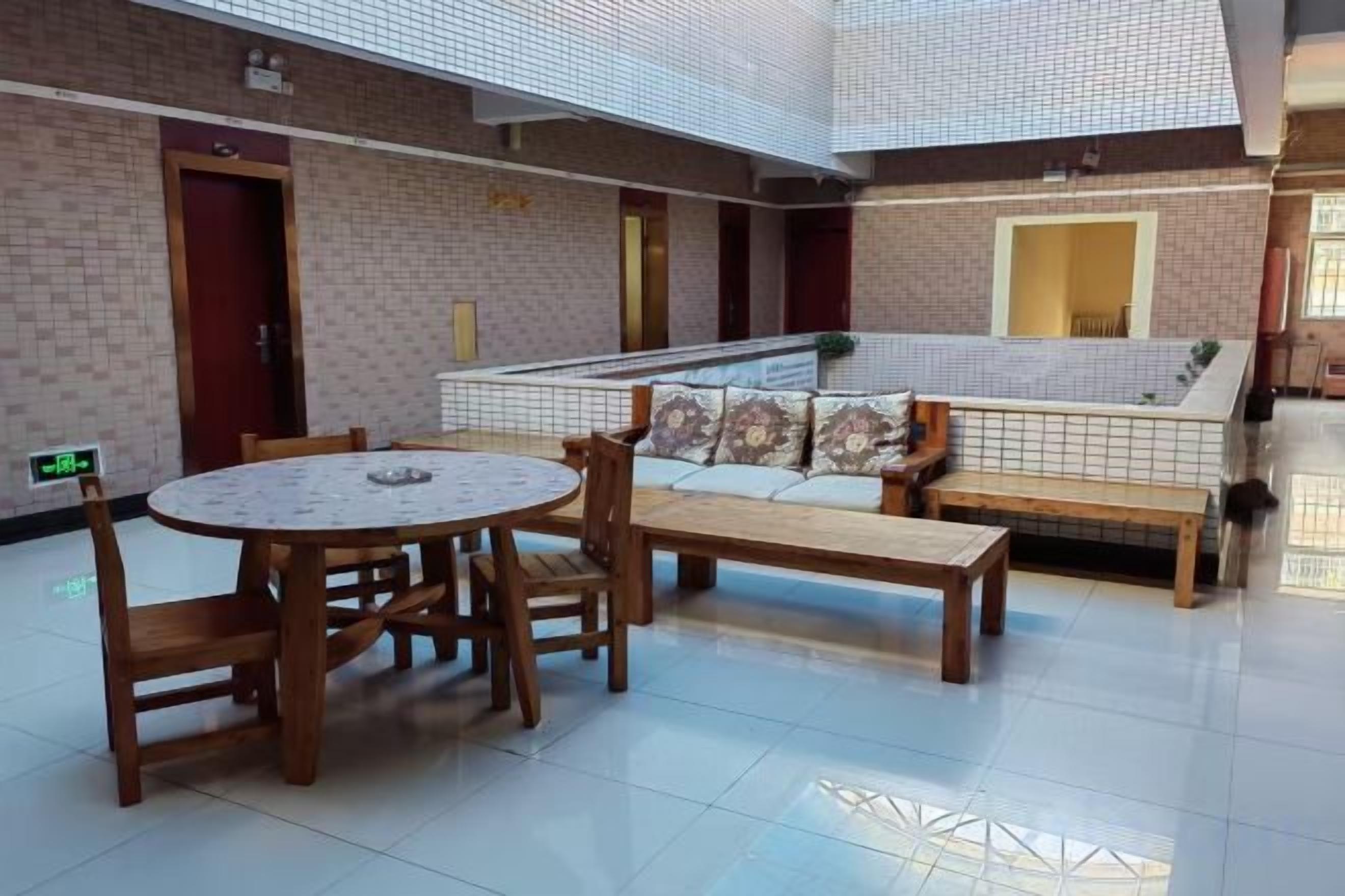 Um espaço amplo e interno, com uma mesa redonda de madeira e cadeiras, um sofá com almofadas e um banco.