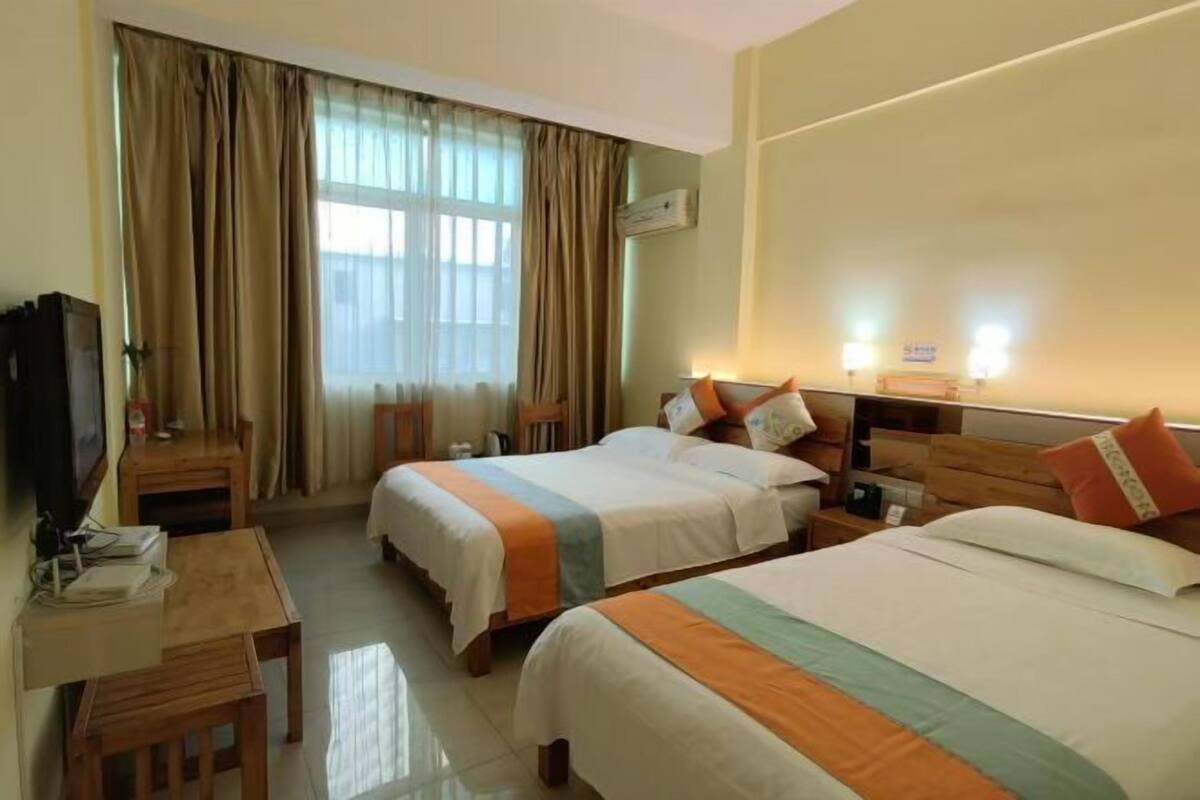 A hotel room with two beds, a desk, a chair, and a television.
