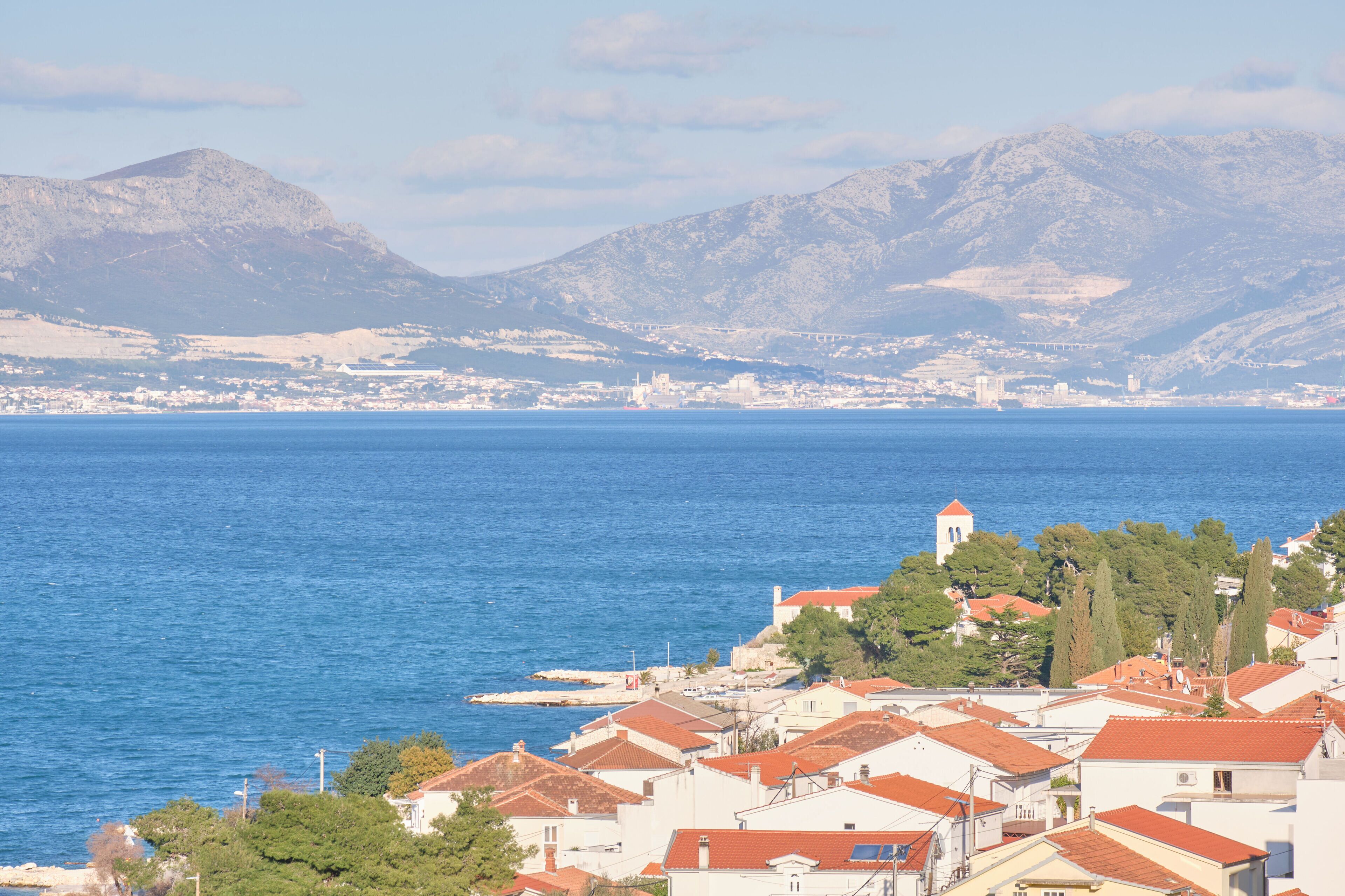 Una cittadina costiera con edifici lungo il lungomare, una montagna imponente sullo sfondo e una vista chiara sul mare.
