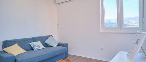 Een moderne woonkamer met een blauwe bank, een klein houten tafeltje, een gekleurd vloerkleed en een raam met uitzicht.