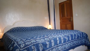 Un dormitorio con una cama cubierta por una colcha azul estampada, una puerta de madera y una mesita de noche con una lámpara.