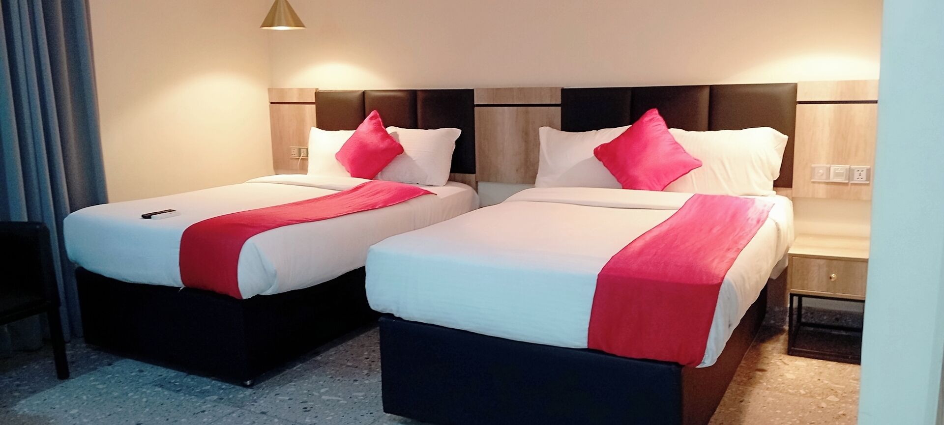 A hotel room with two beds, each with a red and white bedspread, and a wooden headboard.