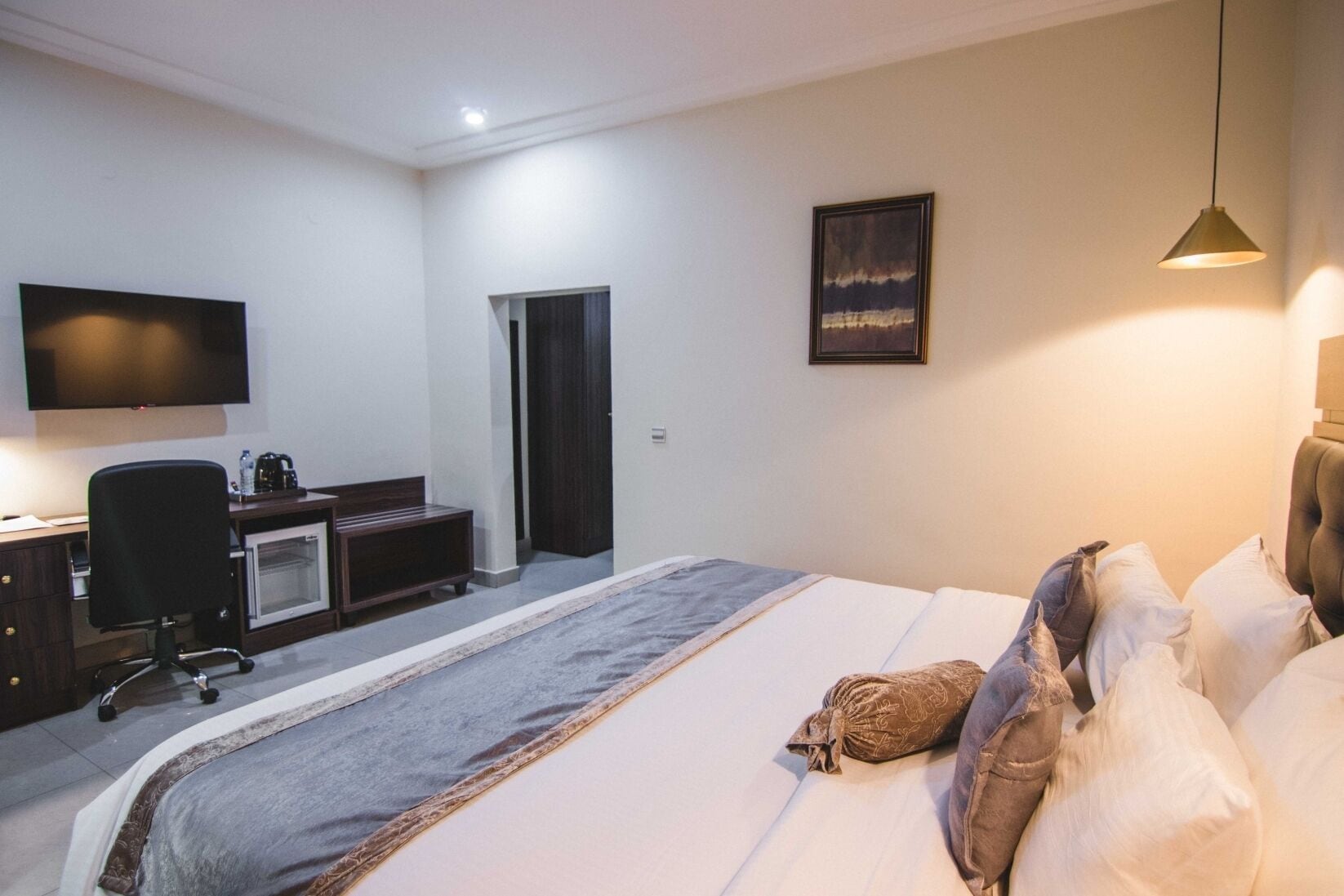 Una habitación de hotel con cama, escritorio, silla, televisor y puerta.