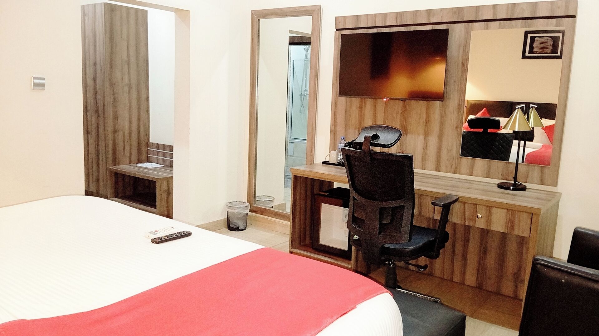 A hotel room with a bed, a desk, a chair, a mirror, and a TV.