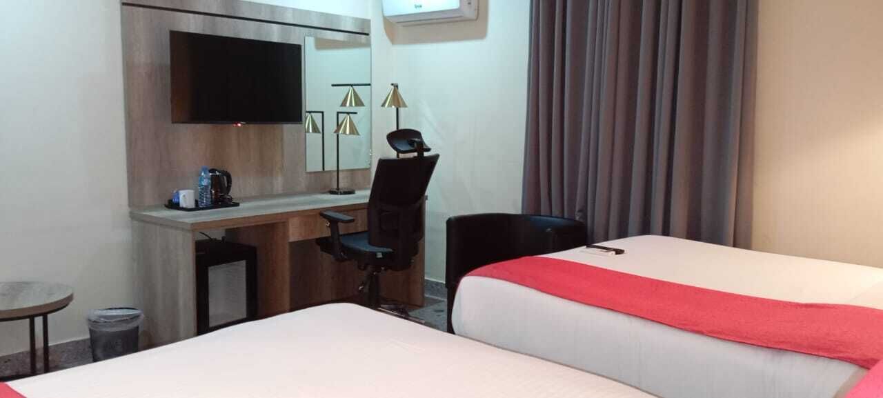 A hotel room with two beds, a desk with a chair, a television, and a small table with a coffee maker.