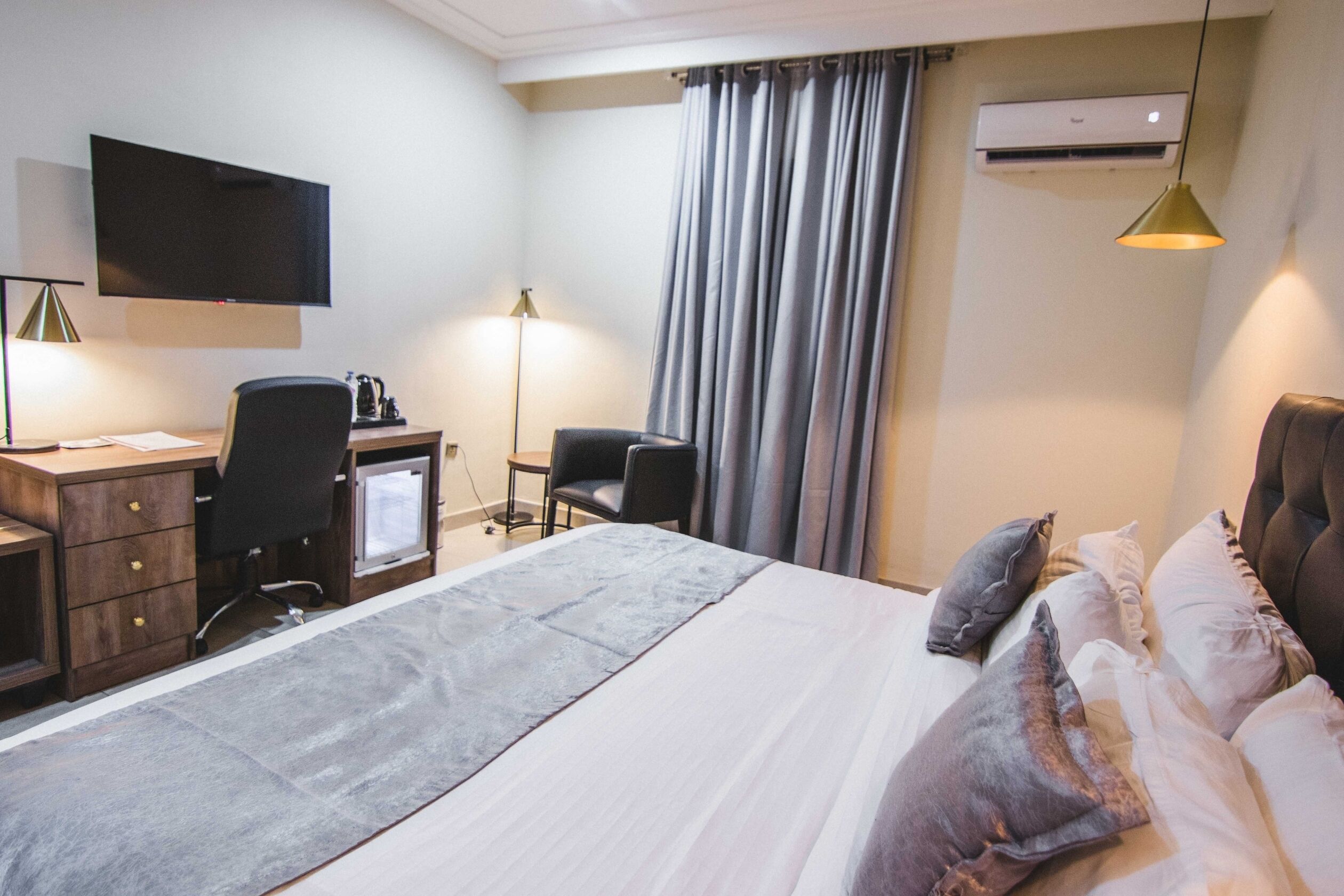 Een hotelkamer met een bed, bureau, stoelen, een flatscreen televisie, een airconditioner en een lamp.