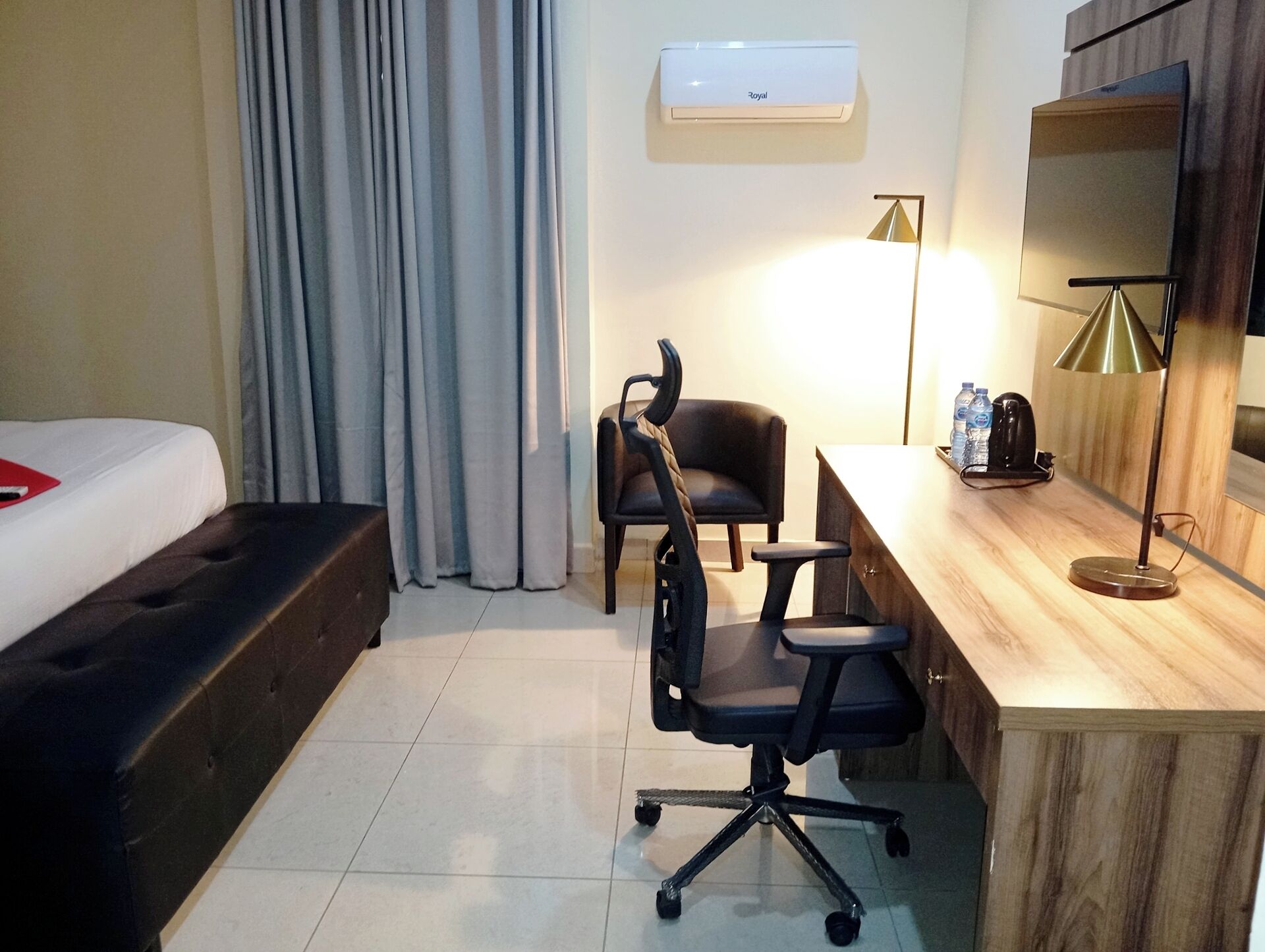 A hotel room with a bed, a desk, a chair, an air conditioner, and a TV.