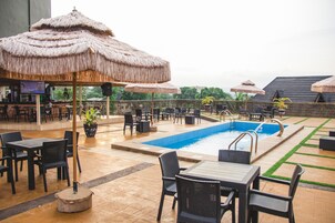 Zona de piscina al aire libre con sombrillas de paja, sillones de descanso y un bar.