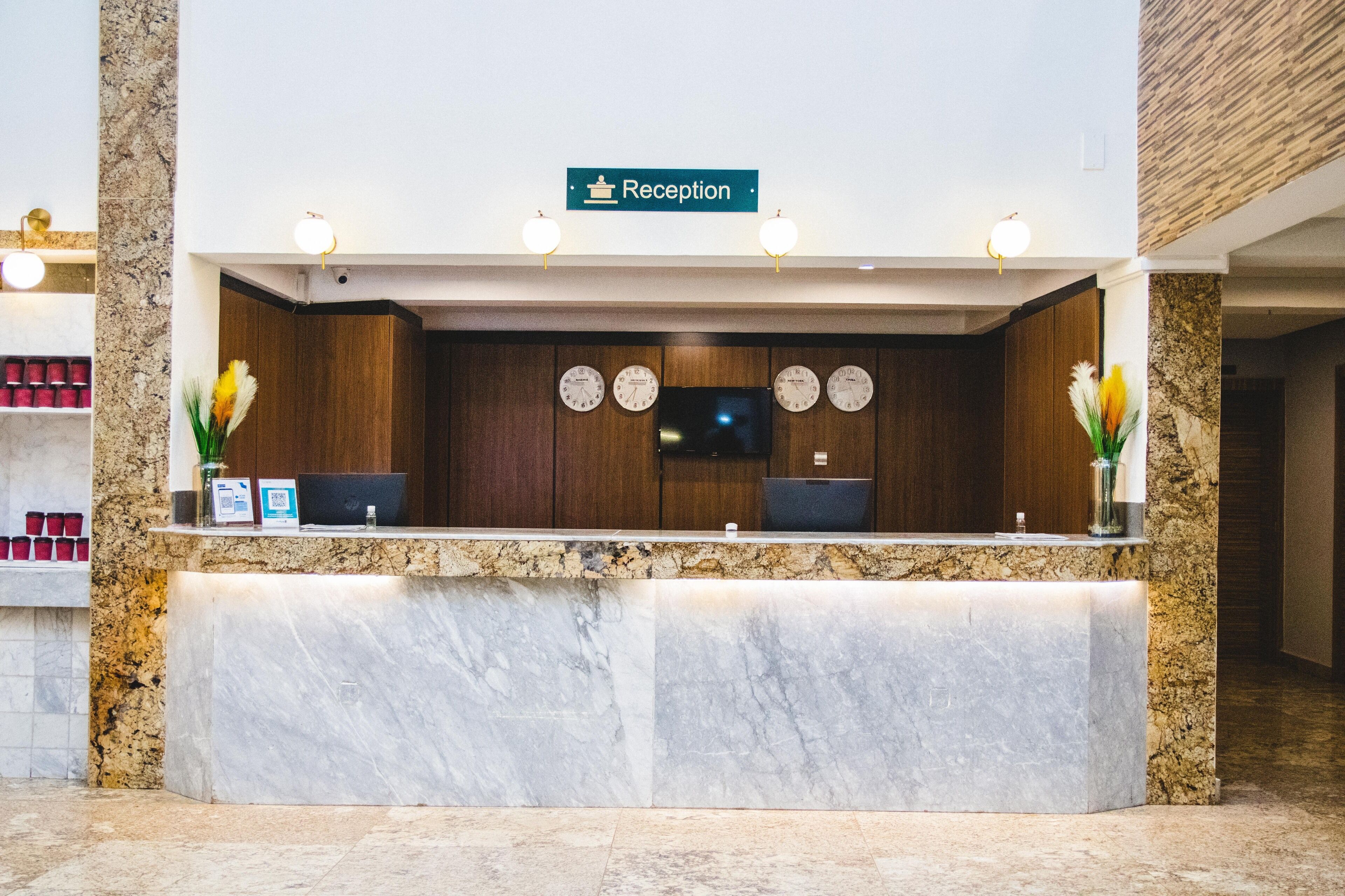 A reception desk with a reception sign, two clocks, and a flat-screen TV.
