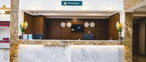 A reception desk with a reception sign, two clocks, and a flat-screen TV.