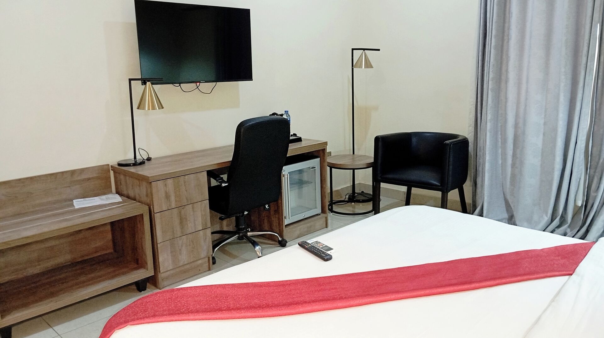A hotel room with a bed, a desk, a chair, a TV, and a small fridge.
