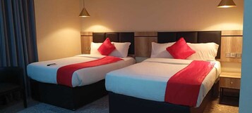 Habitación de hotel con dos camas, cada una con un edredón rojo y almohadas blancas.