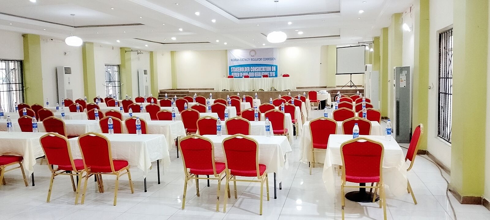 A conference room with rows of tables and chairs, a podium, and a banner for a stakeholder consultation.