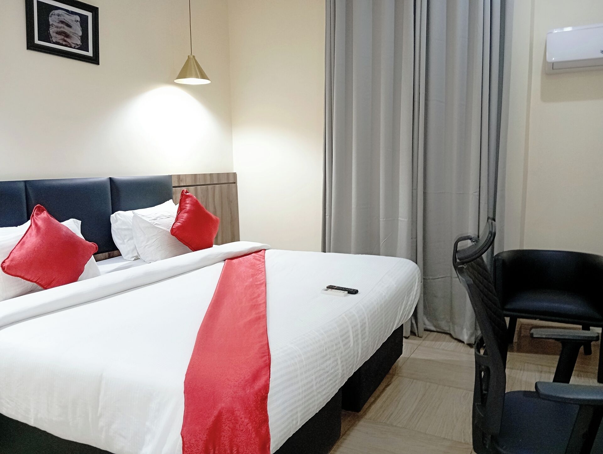 Een netjes opgemaakt bed met witte en rode beddengoed, een zwarte stoel en een hangende hanglamp.