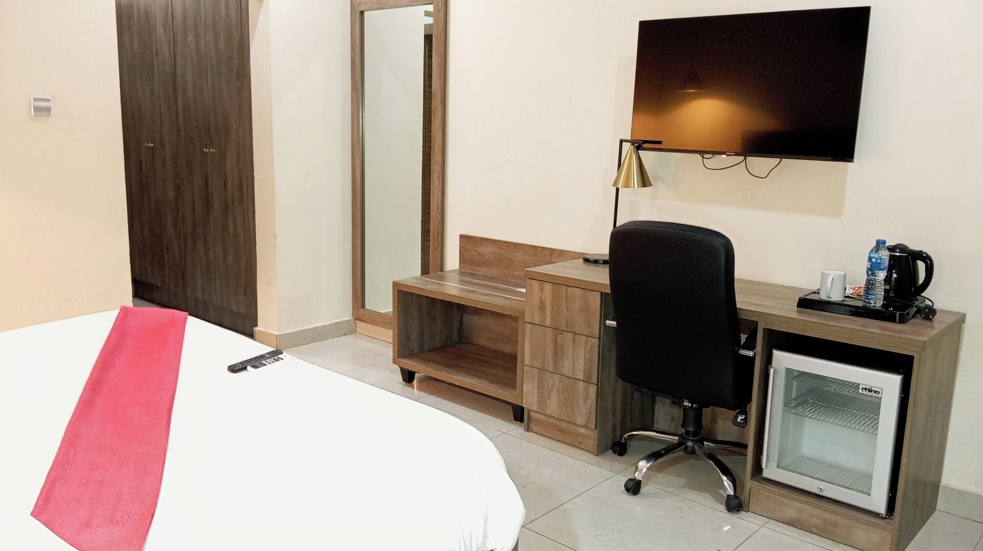 A hotel room with a bed, a desk with a chair, a television, a coffee maker, and a mini-fridge.