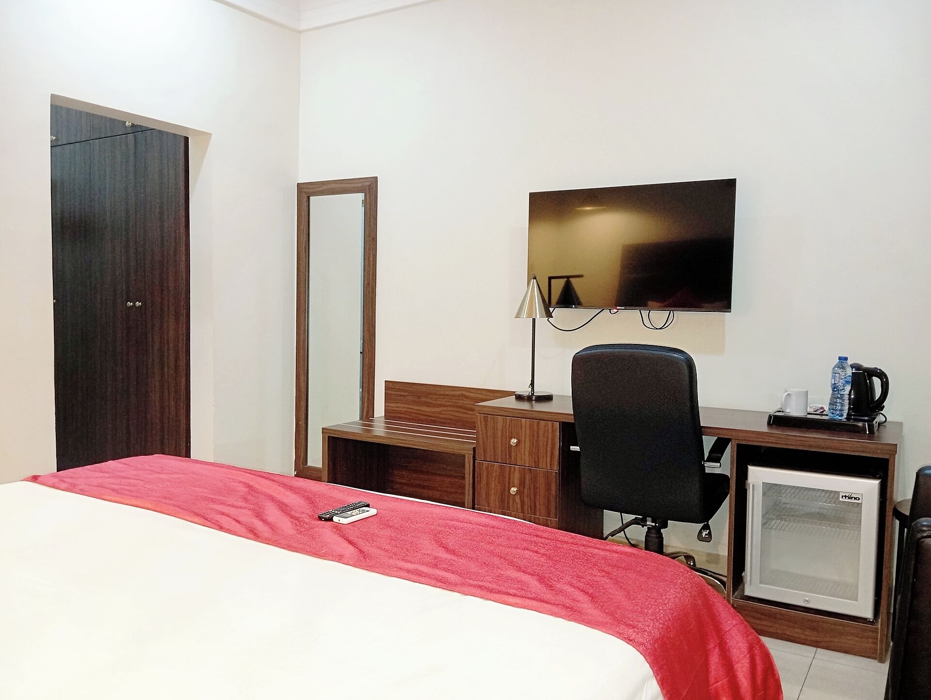 Habitación de hotel con cama, escritorio, silla, televisor, refrigerador pequeño y armario.