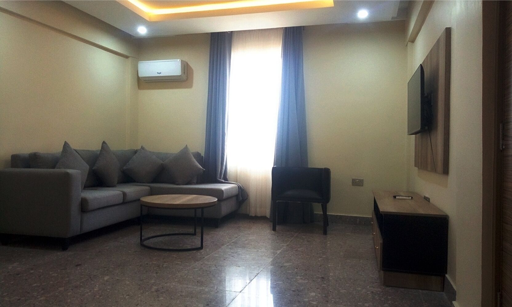 A living room with a sofa, a coffee table, a chair, a TV, and a window with curtains.