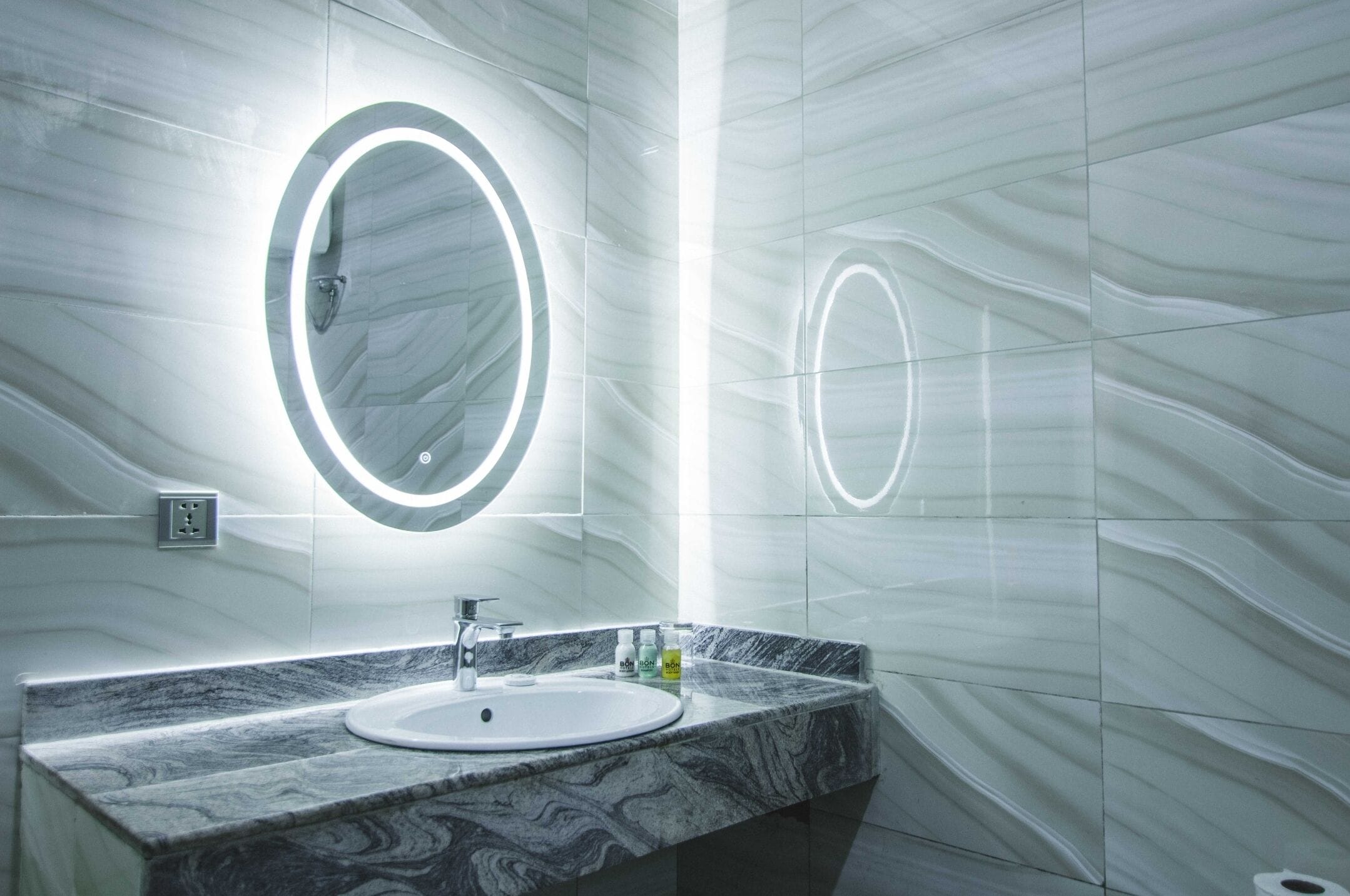 A modern bathroom with a marble sink, two illuminated mirrors, and a marble countertop.