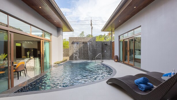 Ein moderner Poolbereich im Freien mit integriertem Wasserrutschen, einem wintergartenartigen Essbereich und einer Liege mit Handtüchern.