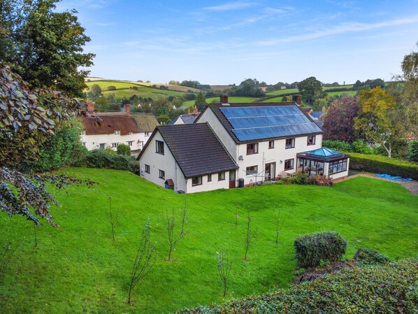 A house with a sloped roof, a conservatory, and a well-maintained lawn.