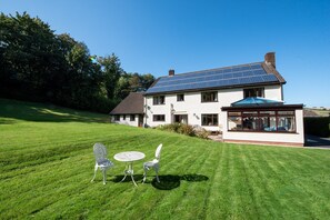 A house with solar panels, a lawn, and a patio with chairs and a table.