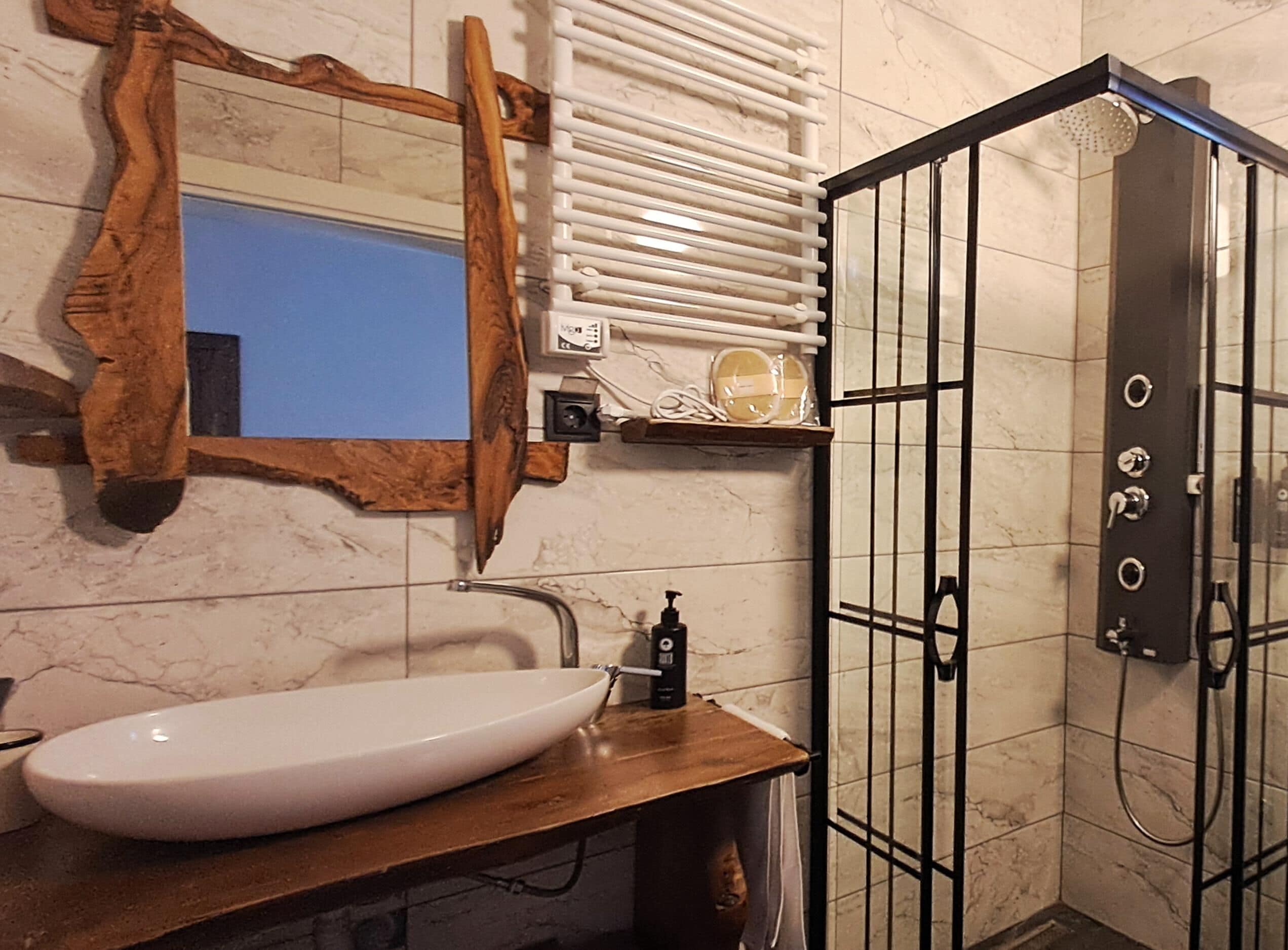 A bathroom with a wooden vanity, a white sink, a mirror, and a shower enclosure with a black door.