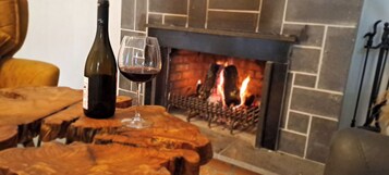 Una mesa de madera con una botella de vino y una copa, una chimenea encendida y una pared de ladrillo.