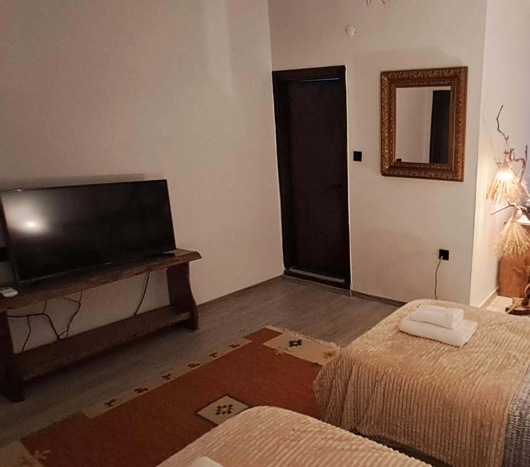 Habitación de hotel con una cama, una mesita de noche con televisor, una puerta y un espejo en la pared.