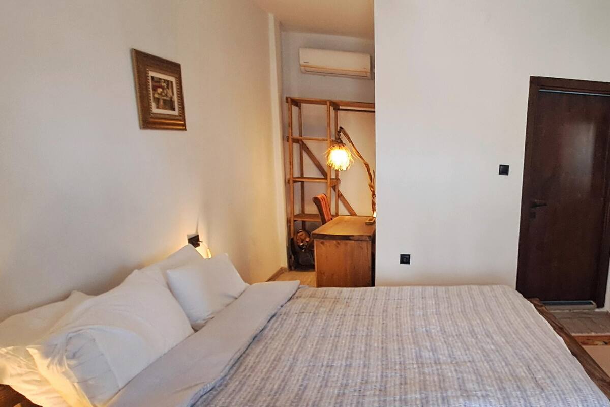 A bedroom with a bed, a wooden chair, a desk, and a lamp.