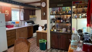 Une cuisine de taille réduite, avec des meubles de rangement en bois, un réfrigérateur, un évier et une horloge au mur.