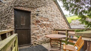 A stone cottage with a wooden door, a small table with chairs, and a wooden bench.