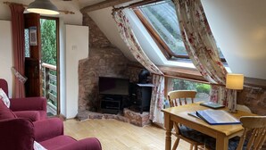 A cozy room with a stone wall, a wooden table, a red sofa, and a television.
