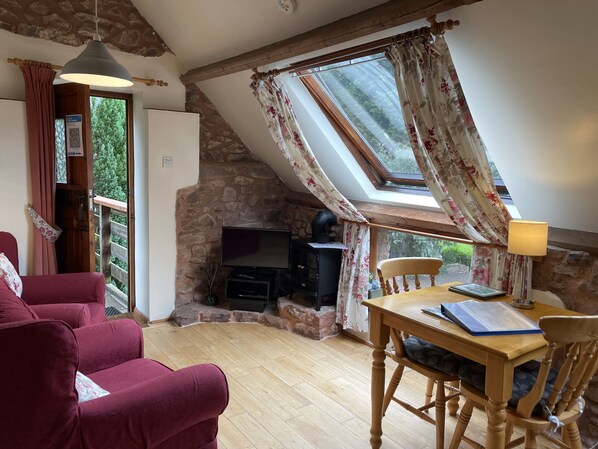 A cozy room with a stone wall, a wooden table, a red sofa, and a television.